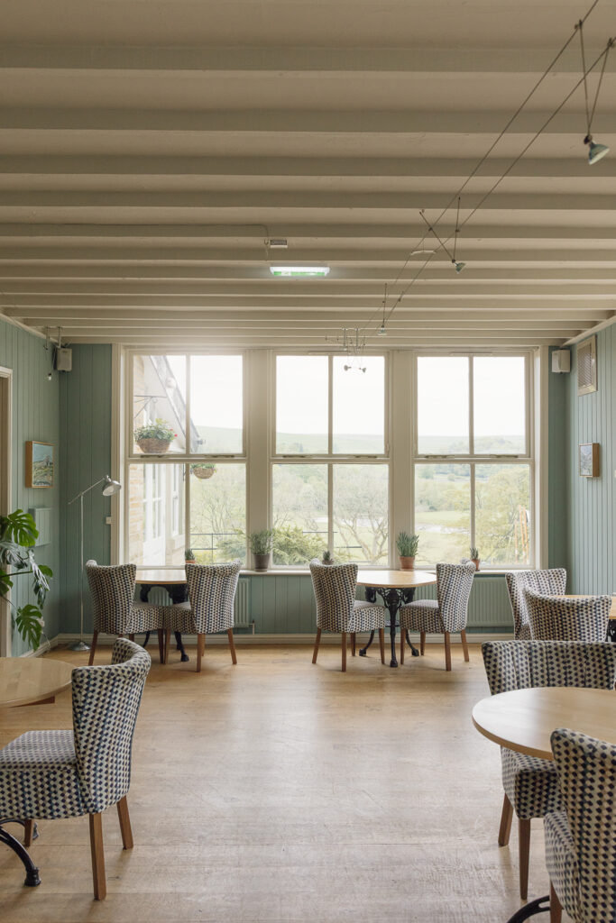 Large white sash windows letting in natural light over wooden tables set for dinner.