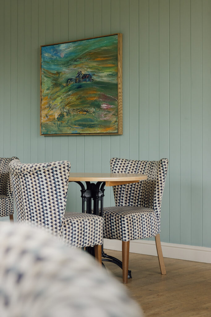 A bistro setting with a green panelled wall behind and a large landscape canvas,