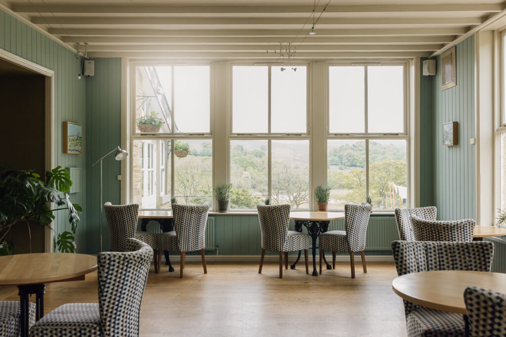Large white sash windows letting in natural light over wooden tables set for dinner.