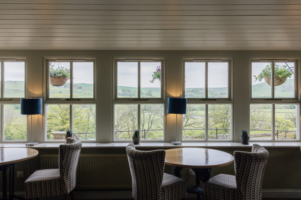 Two tables with checked chairs sat behind large white sash windows looking out on the dales.