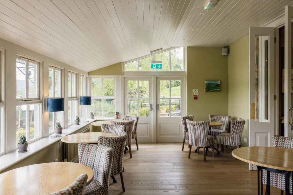 Conservatory dining room at The Fell Hotel near Bolton Abbey, featuring large windows, wooden floors, and views across the Yorkshire Dales valley.