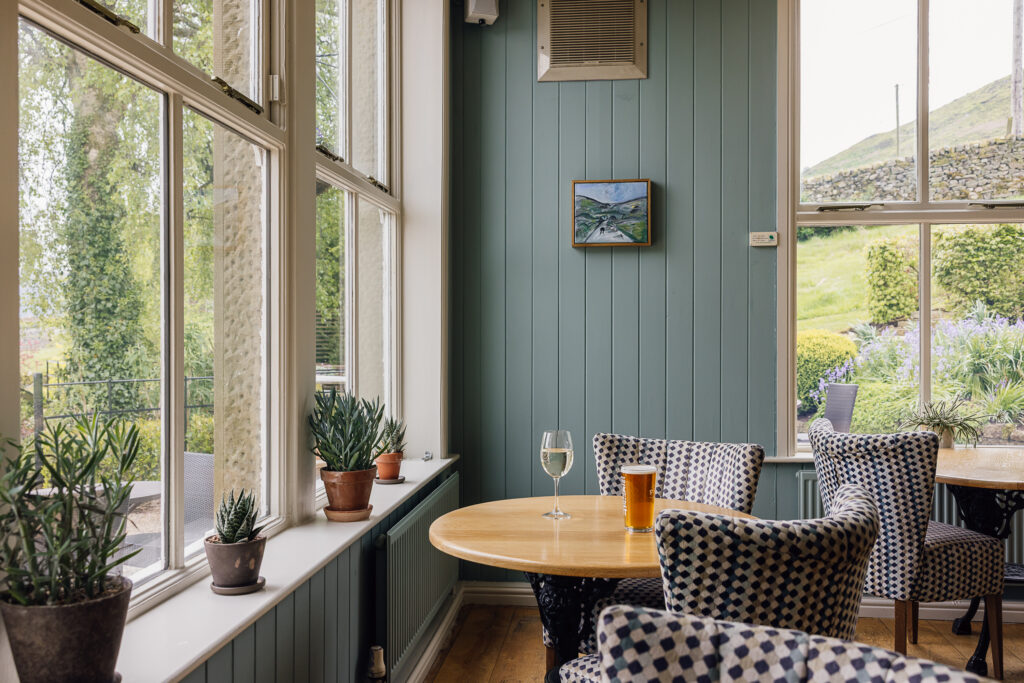 A draught beer, and a glass of white wine sat on a wooden table with checked chairs.