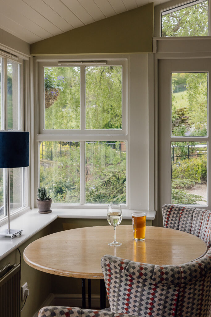 A glass of white wine and draught beer sat on a table with checked chairs behind. White sash windows either side of the conservatory.