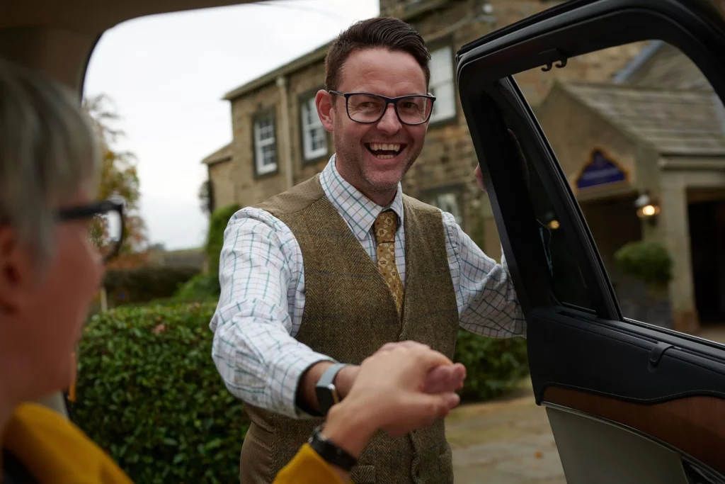 Man holding door open of a car whilst smiling