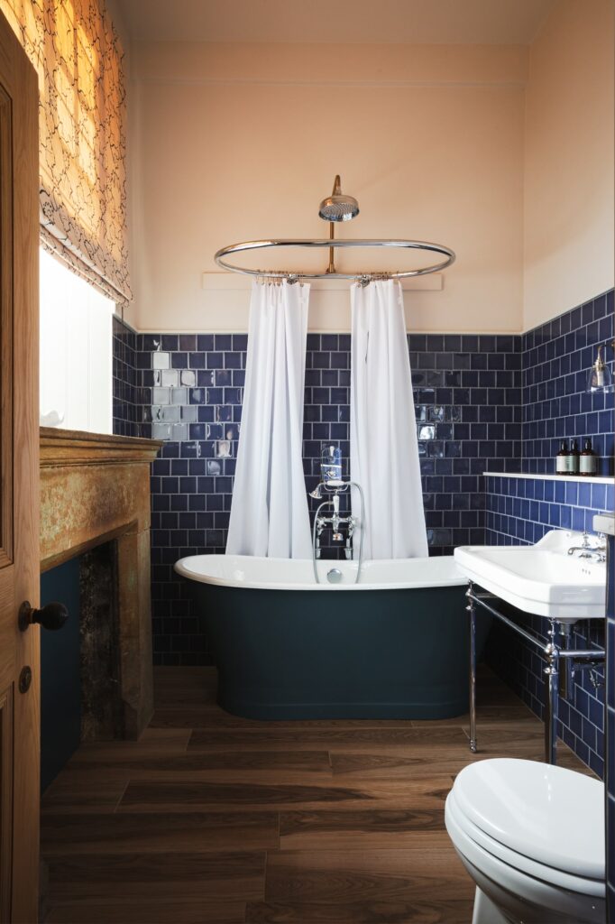 A blue-tiled bathroom with a roll-top bath and rustic fireplace.