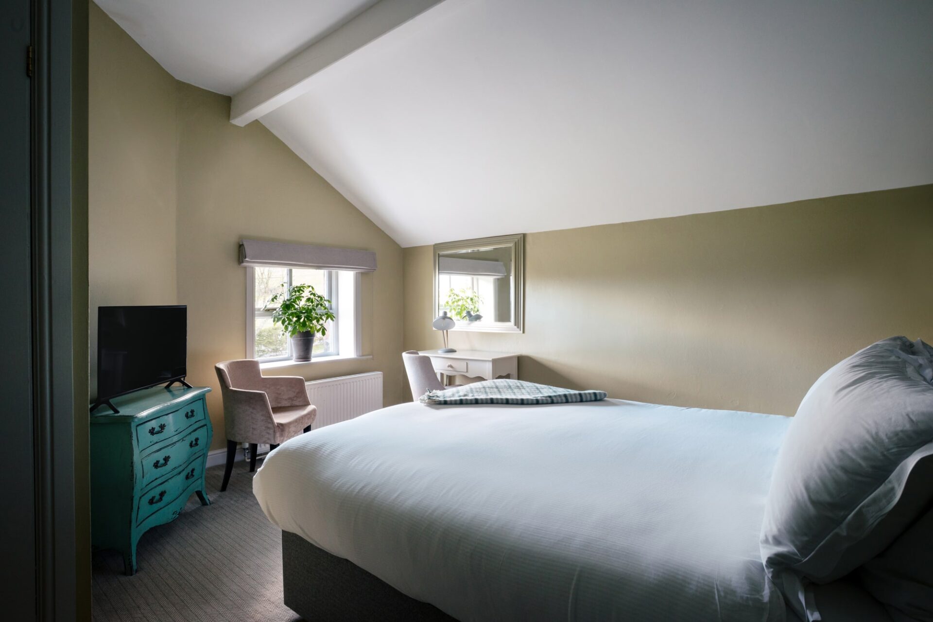 A green-coloured bedroom with double bed and plant on the windowsill.