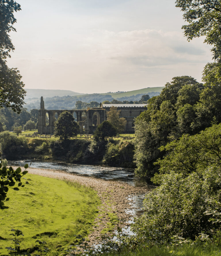 The Priory of bolton abbey peeping through the trees with the river wharfe infront.