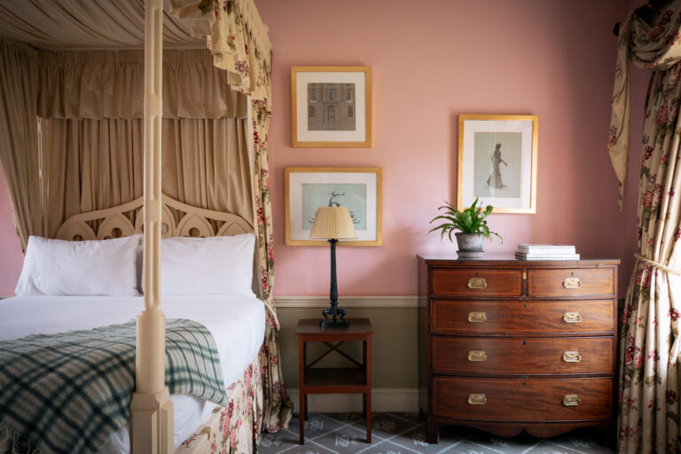 A fourposter bed in a pink room with antique furnishings.