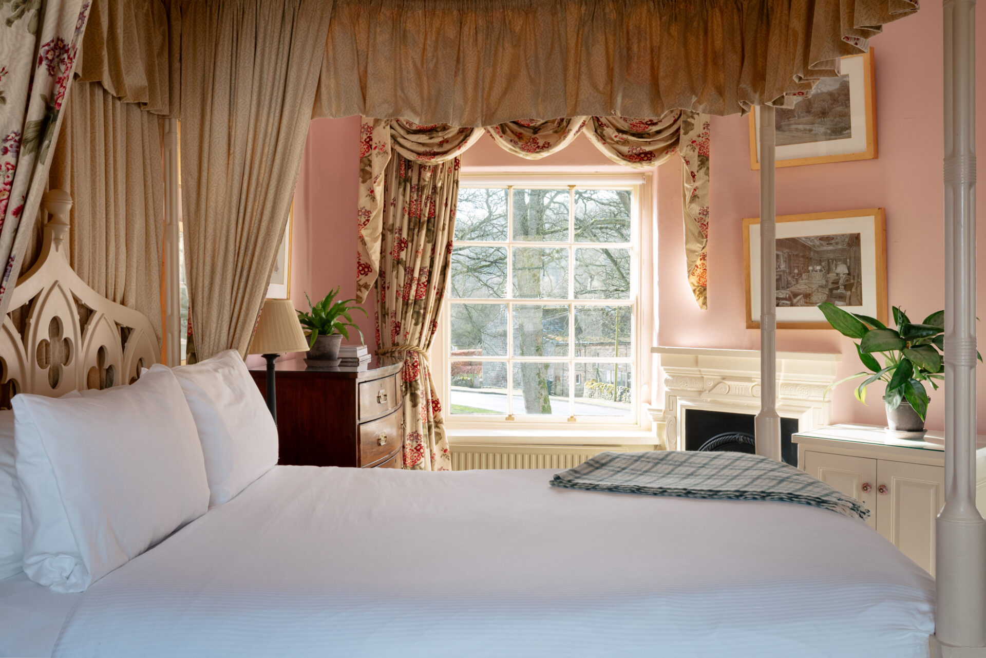 A fourposter bed in a pink room with antique furnishings.