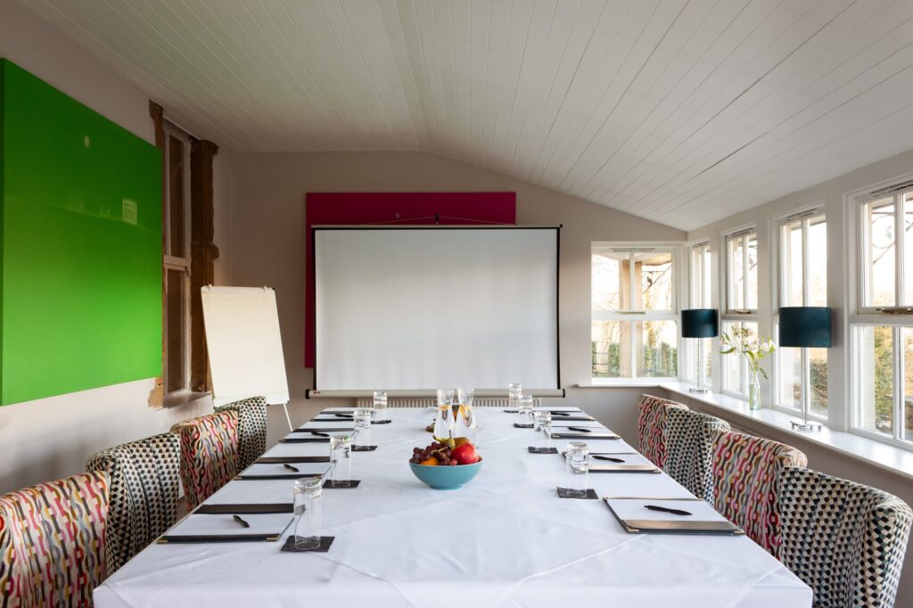 A corporate table set up in the conservatory with large green and pink paintings and screen.