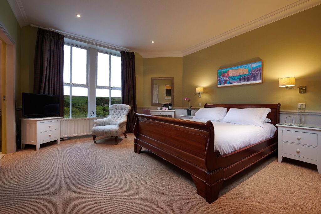 A green bedroom with large brown sleigh bed with purple curtains and artwork.