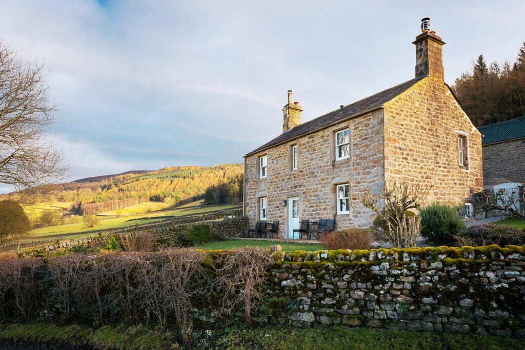 Exterior of the old farmhouse cottage, with stone work and the valley in the background.