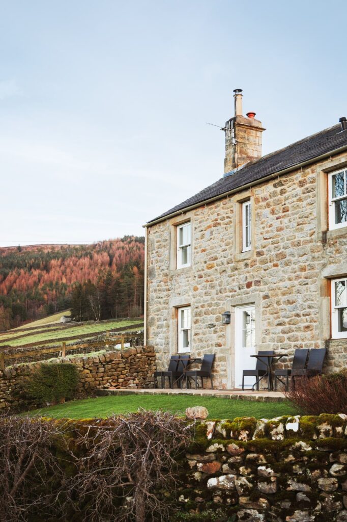 Exterior of the farmhouse cottage with outdoor seating and the garden area shown, with the forest in the background.