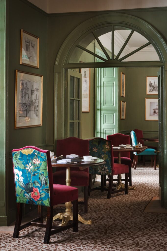 A green dining area with red floral chairs and tables set up for breakfast.