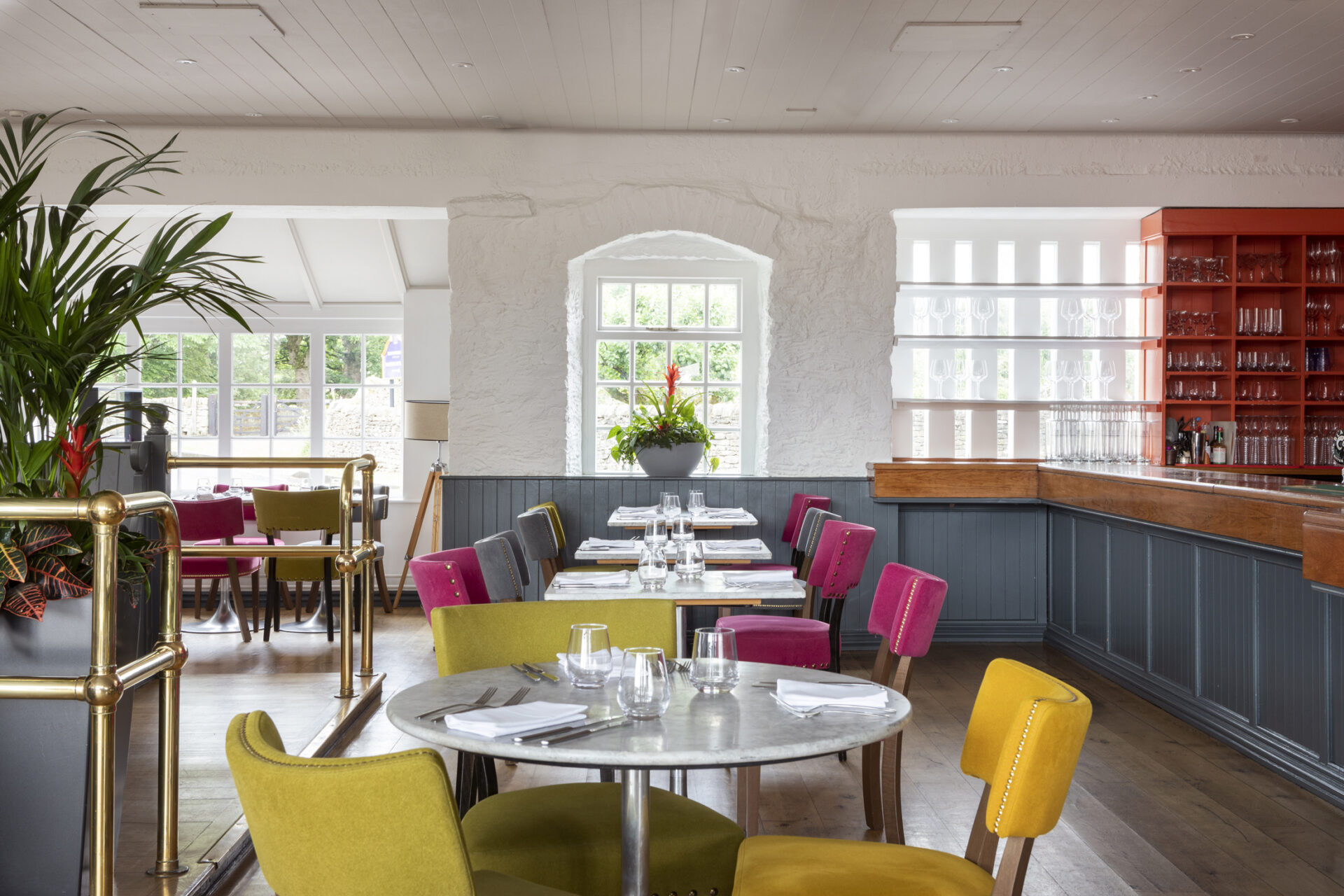 A large room set with colourful dining chairs and tables, with open windows and plants.