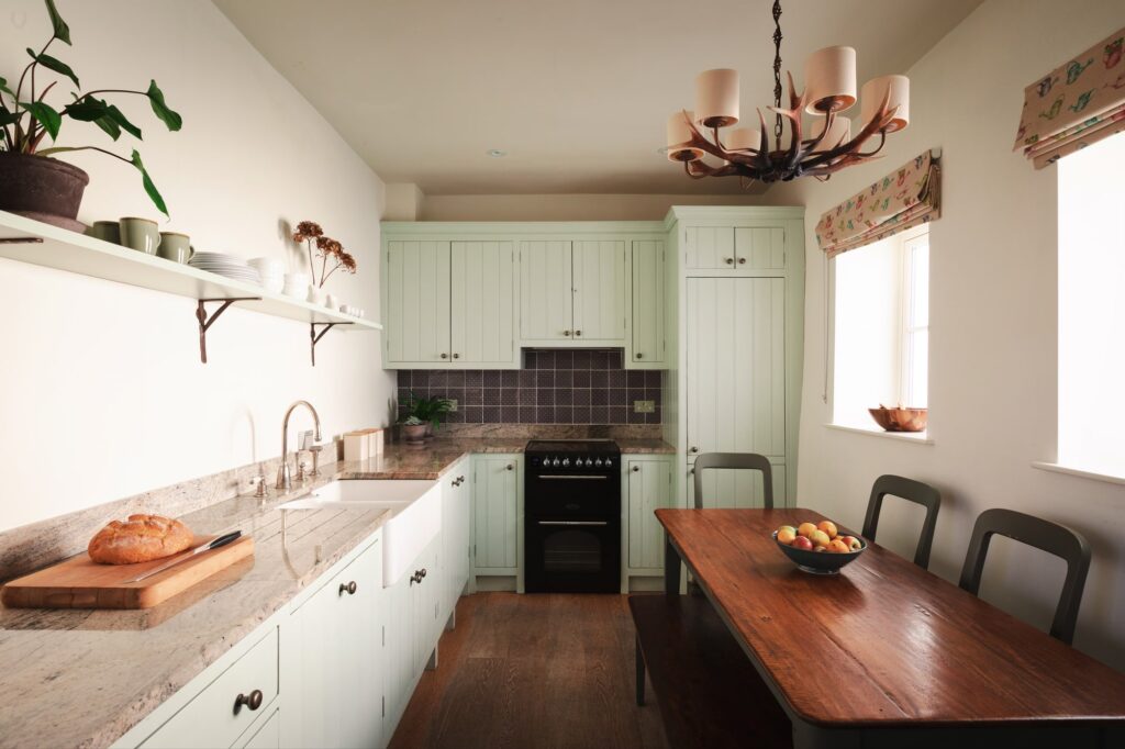 Traditional farmhouse kitchen dining room, with green cupboards and oak table and bench.