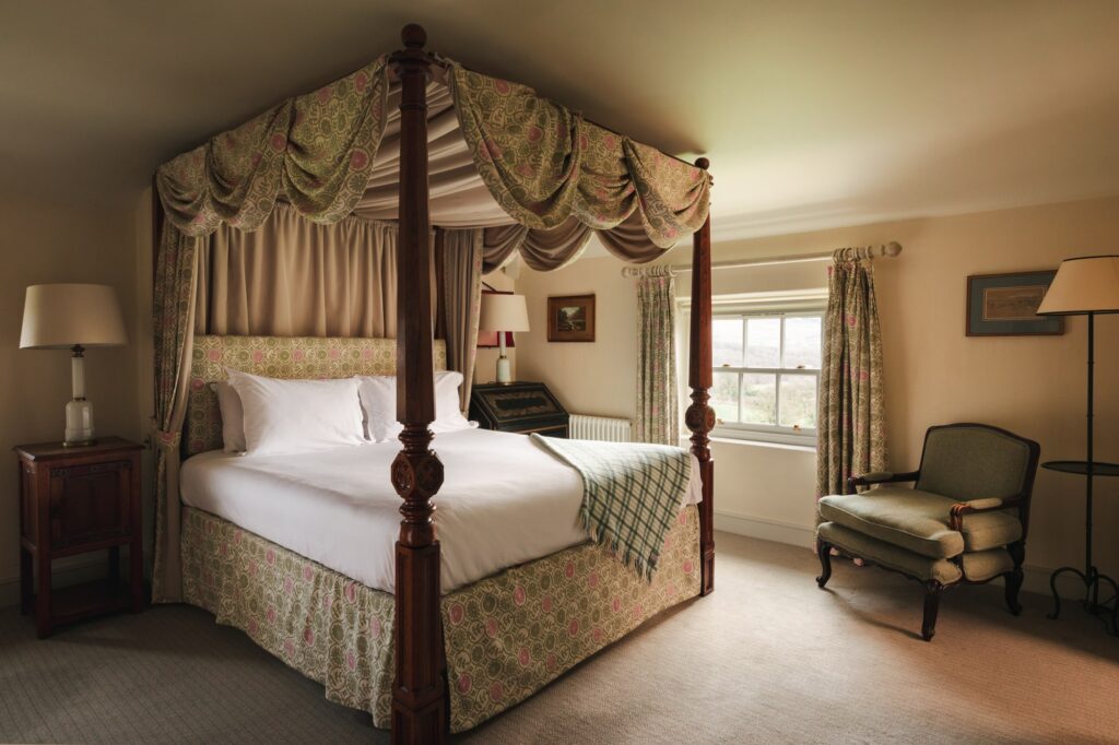 Large four-poster bed in the main bedroom, with floral covers and draped curtains.