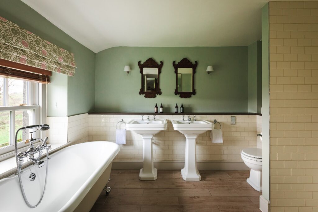 Large bathroom with roll top bath, shower and two sinks with antique furnishings.