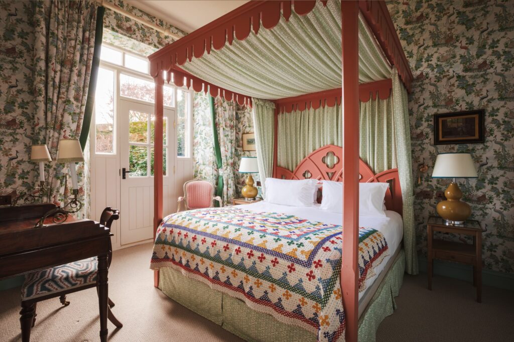 A floral four-poster bed, with pink frame and eclectic wallpaper.