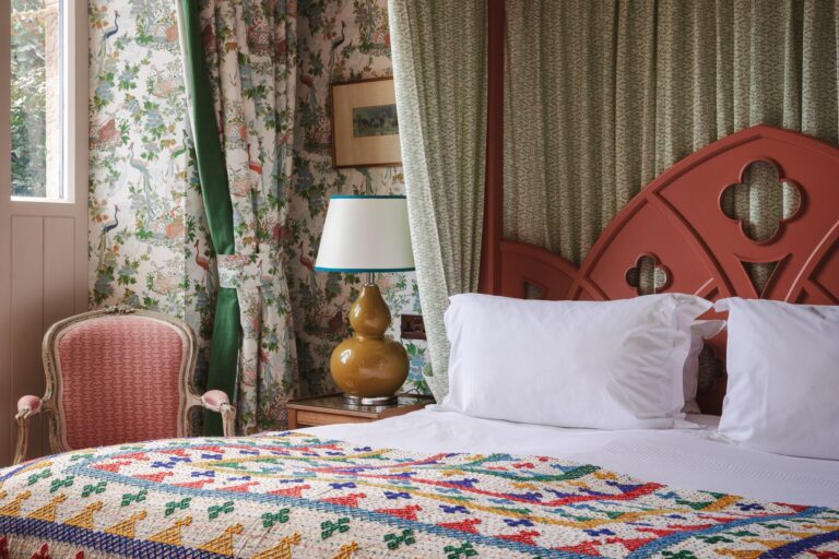 Close-up of the four-poster bed with floral wallpaper and door outside.