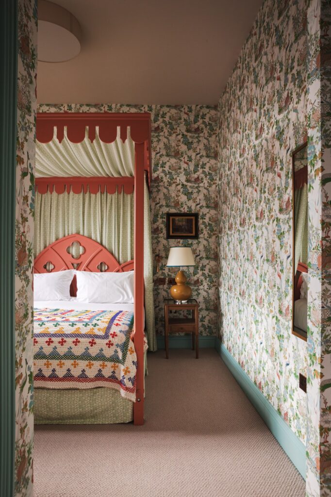 The hallway looking through to a pink four-poster bed with floral wallpaper.