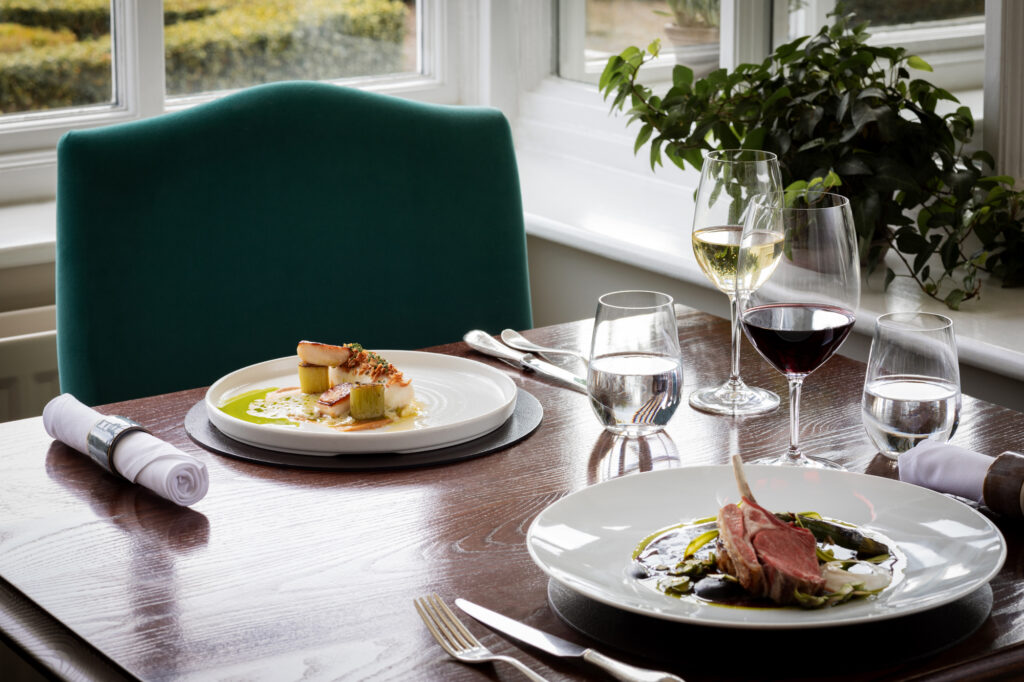 A table of food with cutlery and napkins, white and red wine and a green chair.