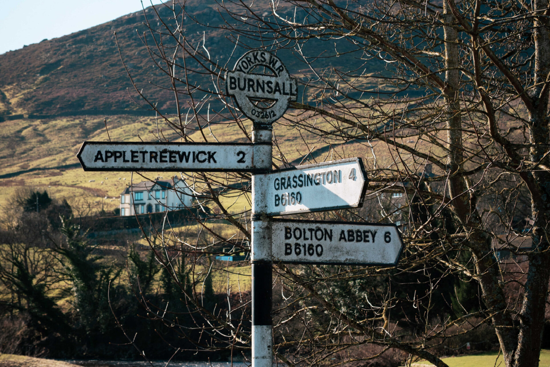 An old fashioned signpost for the Yorkshire Dales, with nearby town names with black and white stripes and the rolling hills beyond.