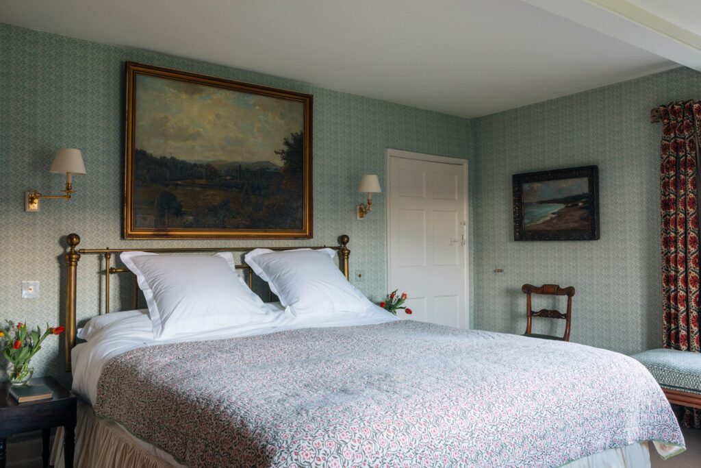 A room with a double bed, blue wallpaper and antique furnishings and oil paintings.