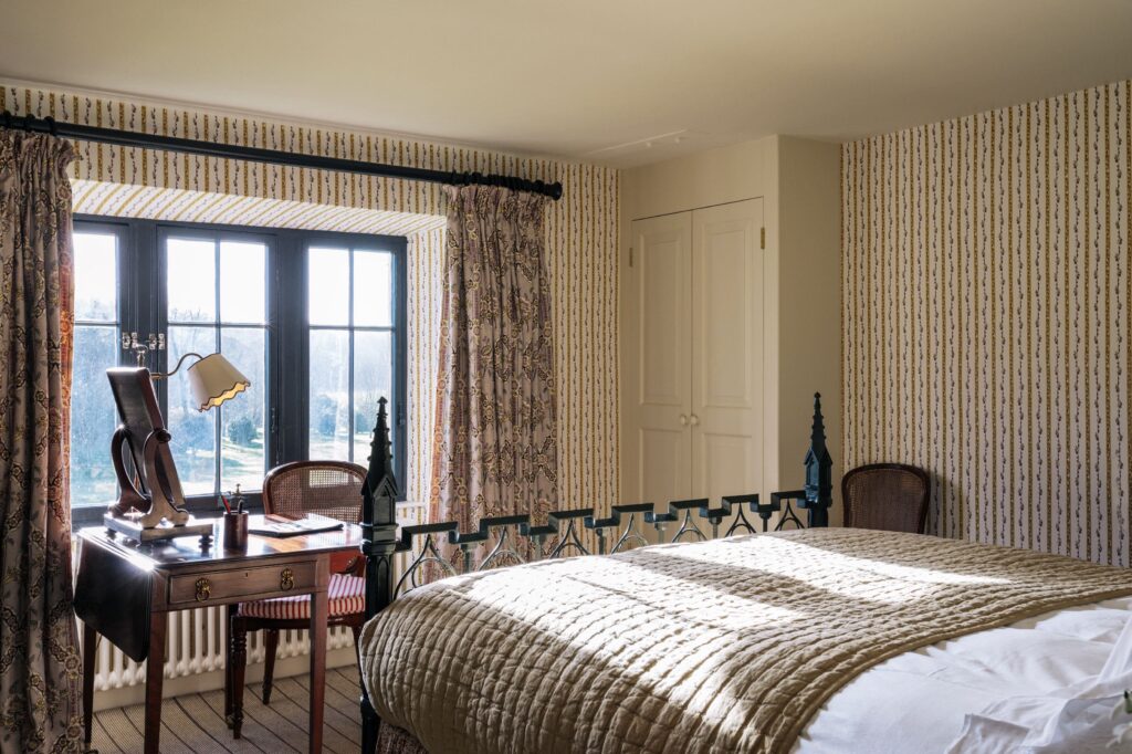 A castle bed is in a beige room with strappy wallpaper with an old wood desk.
