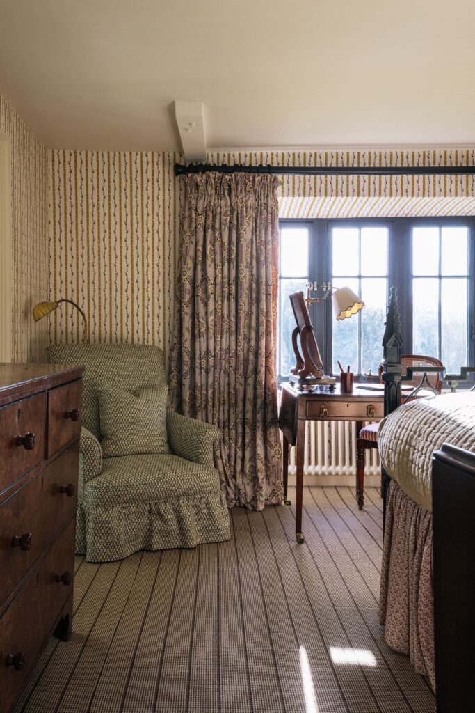 An armchair sits in the corner of a stripy room with an old oak chest of draws nearby,