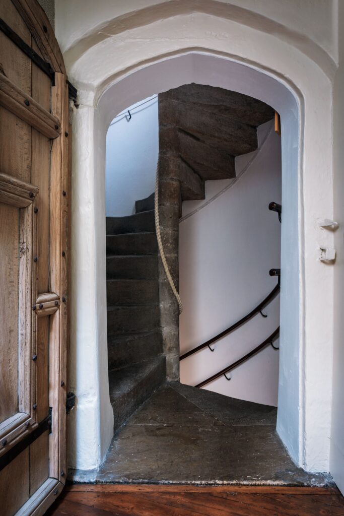 An ancient stone spiral staircase through the castle, with iron hand rails and wooden door.