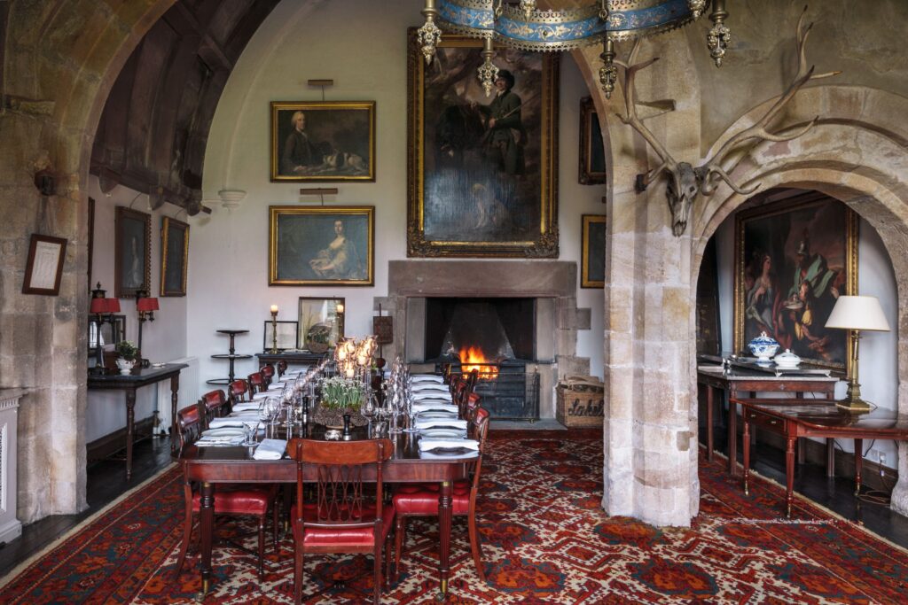 A large dining table, surrounded by old oil paintings with fire nearby.
