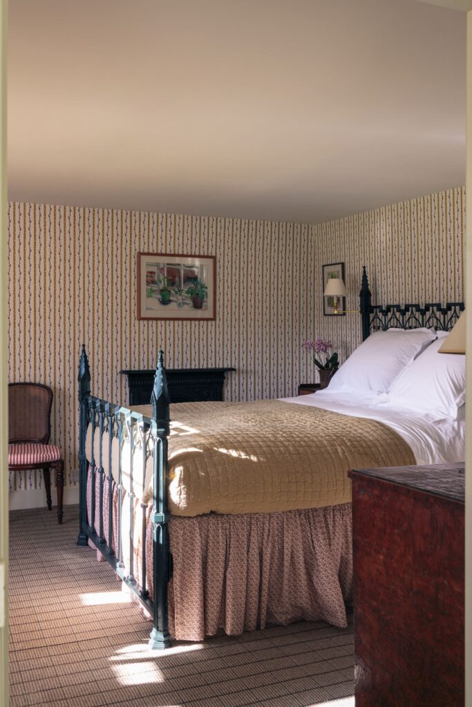 A beige stripy bedroom with a castle bed and beige covers wit oak draws.