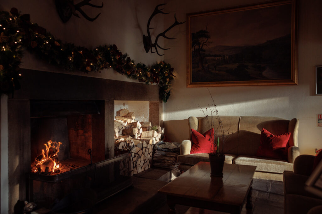 A sofa by a large roaring fire, garland attached to the wall above.