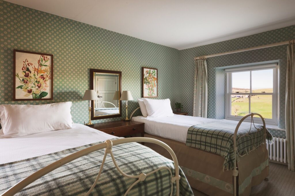 Twin room with floral artwork, check throws and blue polka dot wallpaper, with a window looking at the view.