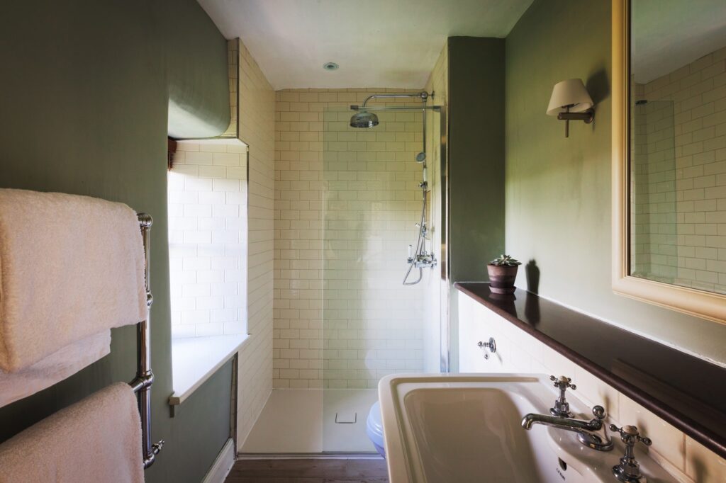 A green bathroom with walk-in shower and white tiles.