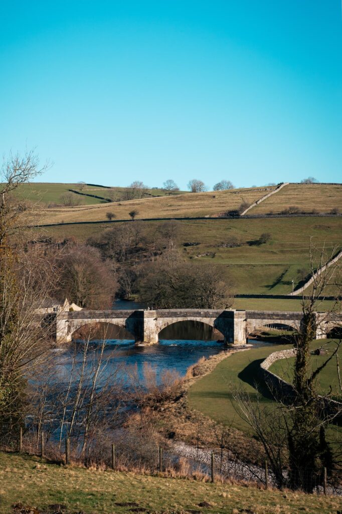 A view from a window onto the valley and the river wharfe below with a bridge over the river and the rolling hills in the background.