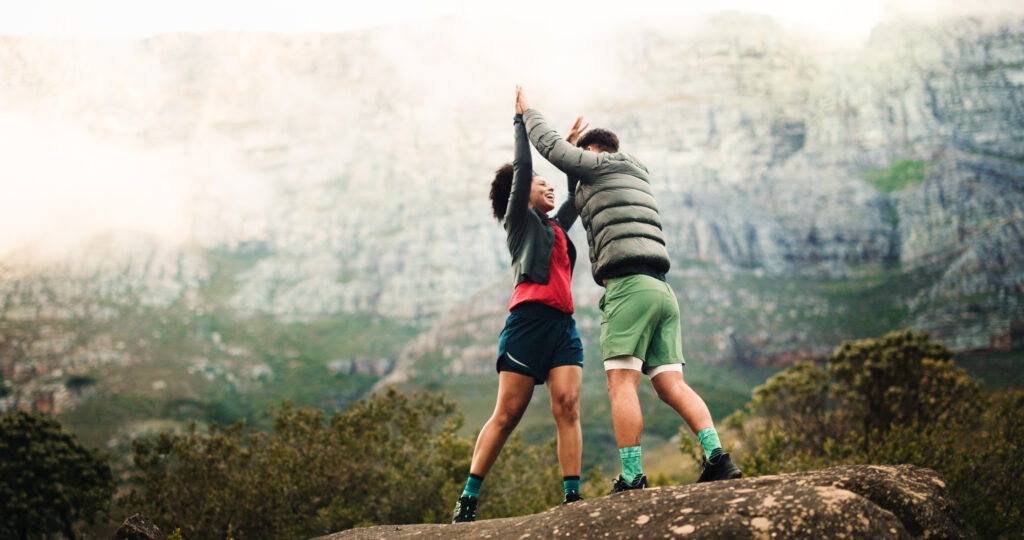 High five, hiking and couple with fitness, support and celebration with relationship. Space, man and woman with goals, challenge or trekking together with nature, travel or explore with achievement.