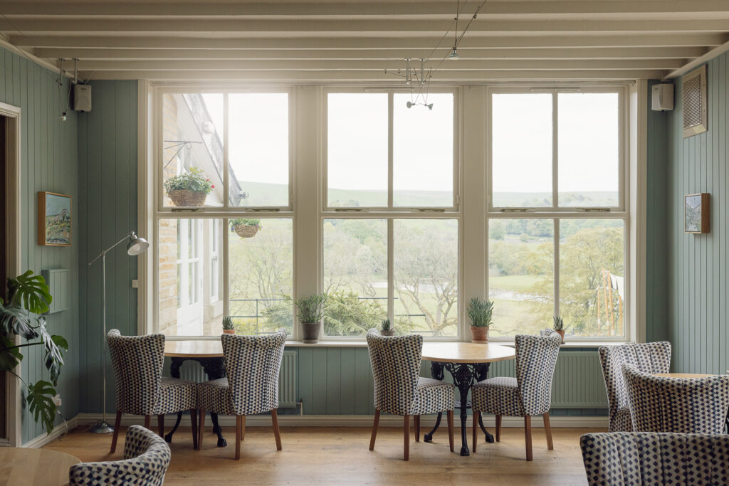 A bistro setting with green walls looking over large sash windows across the Yorkshire Dales.